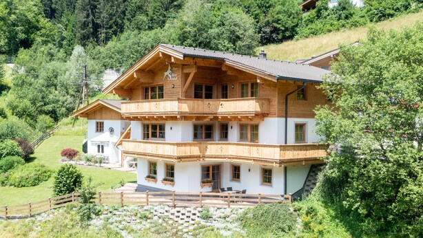 Een chalet van hout met meerdere verdiepingen en balkons, omringd door weelderige begroeiing en een bergachtige achtergrond.