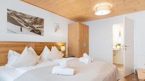 Een hotelkamer met een houten plafond, een bed met witte lakens, een hangend schilderij van een skiër en een houten kledingkast.