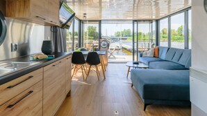Een modern interieur met een keuken, een eetgedeelte en een zithoek, met grote ramen met uitzicht op een waterweg.