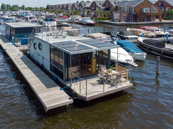 A floating houseboat with a deck and a covered outdoor area, docked at a marina with other boats. - Houseboat with views from the roof terrace (Uitgeest)
