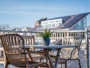 A balcony with wicker chairs and a table, a potted fern, and a view of buildings in the background. - Houseboat with views from the roof terrace (Uitgeest)