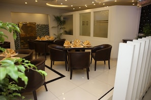 A modern dining area with a round table set for four, surrounded by dark leather chairs. A large potted plant is visible in the foreground. - Fort Continental Hotel (Peshawar)