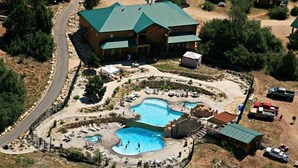 A large building with a green roof, surrounded by a swimming pool area with multiple pools and sun loungers. - Zion Cabin Retreat - Luxury with Nature Trails in Uncrowded East Zion. 3 kings (Orderville)