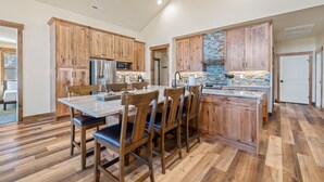 A spacious kitchen with wooden cabinets, a large island, and a stone backsplash. - Zion Cabin Retreat - Luxury with Nature Trails in Uncrowded East Zion. 3 kings (Orderville)