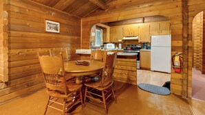 A wooden cabin interior with a dining table, chairs, a kitchen area, and a fire extinguisher. - Cedar Cabin Near Mount Rainier, Cozy Forest Stay for 4 (Ashford)