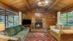 A cozy cabin interior with a fireplace, leather sofas, and large windows overlooking a forest. - Cedar Cabin Near Mount Rainier, Cozy Forest Stay for 4 (Ashford)