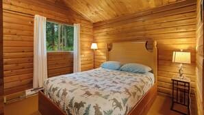 A wooden cabin bedroom with a bed, a nightstand, a lamp, and a window with curtains. - Cedar Cabin Near Mount Rainier, Cozy Forest Stay for 4 (Ashford)