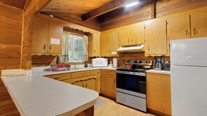 A wooden cabin kitchen with a white countertop, wooden cabinets, a stove, and a refrigerator. - Cedar Cabin Near Mount Rainier, Cozy Forest Stay for 4 (Ashford)