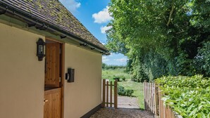 A quaint cottage with a wooden door, a small porch, and a gravel path leading to a wooden gate.