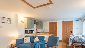 A cozy living room with a blue sofa, wooden dining table, and a kitchen area with teal cabinets and wooden doors.
