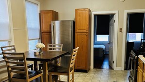 A kitchen with wooden cabinets, a stainless steel refrigerator, a dining table with chairs, and a black mat on the floor. - Apt with utilities, wifi, a compact parking space, & on-site laundry near NYC! (Bayonne)