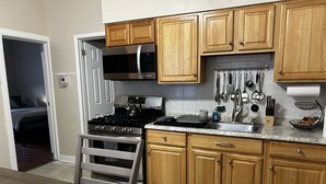 A modern kitchen with wooden cabinets, stainless steel appliances, and a dining area with a bench. - Apt with utilities, wifi, a compact parking space, & on-site laundry near NYC! (Bayonne)