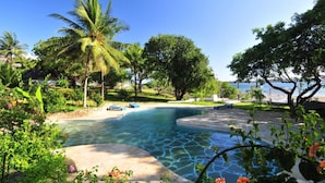 A swimming pool with clear water, surrounded by lush greenery and palm trees. - Shimoni Reef Lodge (Mombasa)