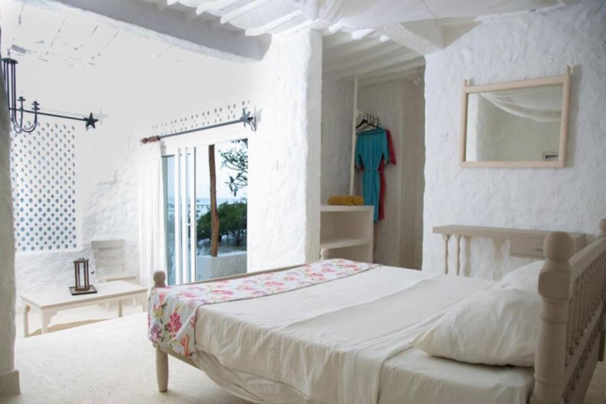 A bedroom with a bed, a window, a hanging light fixture, and a mirror on the wall.