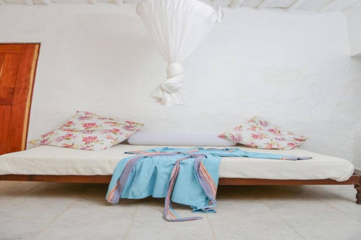 A bed with a white canopy, floral pillows, and a blue blanket.