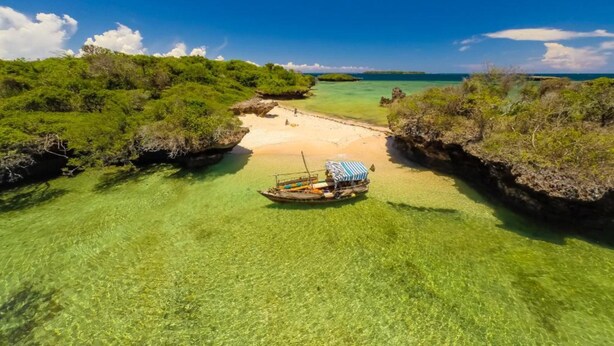 A boat on a clear turquoise sea with a sandy beach and lush greenery. - Shimoni Reef Lodge (Mombasa)