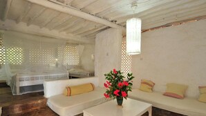 A cozy room with a white sofa, a small table with a vase of flowers, and a bed with a white canopy. - Shimoni Reef Lodge (Mombasa)