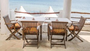 A covered outdoor seating area with a table and chairs, overlooking a body of water. - Shimoni Reef Lodge (Mombasa)