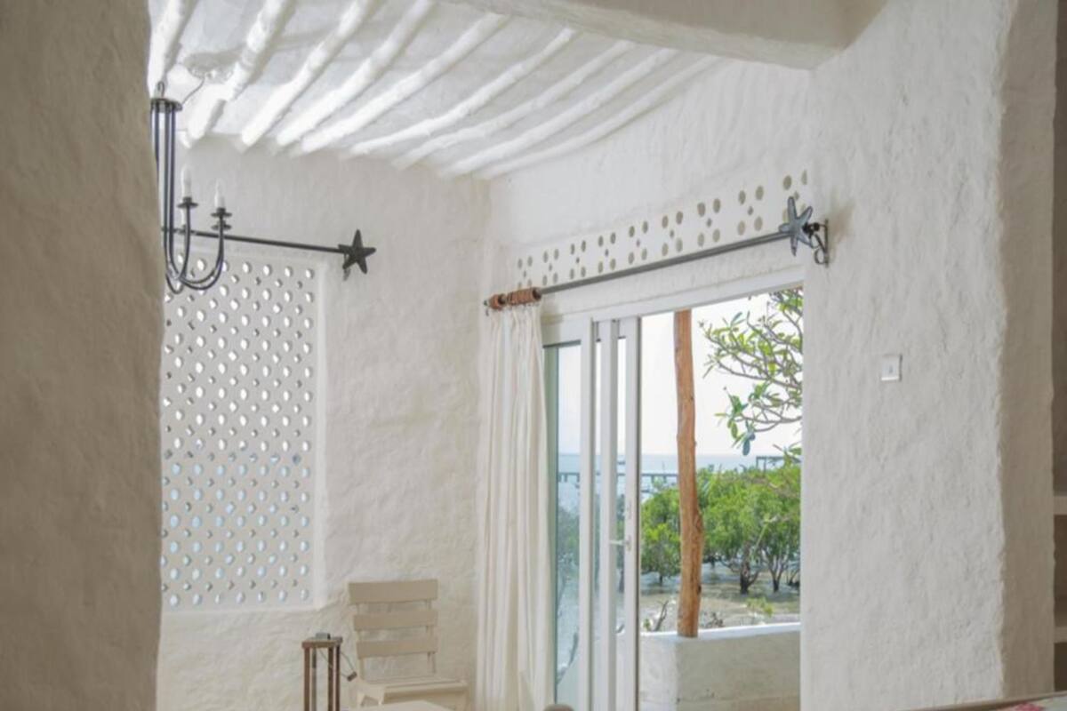 A room with a bed, a table, a chair, a window with a view of trees, and a ceiling with a unique design.