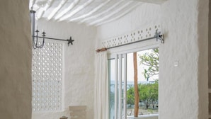 A room with a bed, a table, a bench, a hanging light fixture, and a view of greenery outside. - Shimoni Reef Lodge (Mombasa)