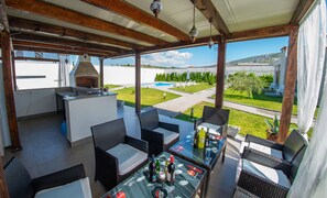 An outdoor patio with a built-in grill, wicker furniture, and a view of a swimming pool and greenery. - Luxury Villa in Mostar (Mostar)