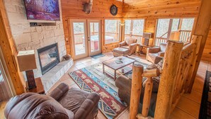 Een gezellig cabin interieur met een open haard, comfortabele zitplaatsen, een opgehangen hertenkop en een groot televisiescherm.
