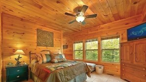 Een slaapkamer in een houten chalet, met een bed, nachtkastje, kapstok en plafondventilator.