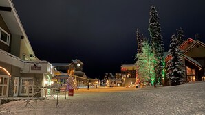 Una calle nevada con edificios, incluyendo el restaurante BullWheel, y un árbol de Navidad con luces.