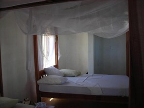 A single bed with white bedding, a wooden headboard, and a mosquito net above. - Morocco House (Lamu)