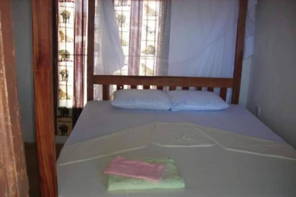 Ein Einzelbett mit weißer Matratze und Kissen, ein Holz-Kopfstück und ein Fenster mit Vorhängen.