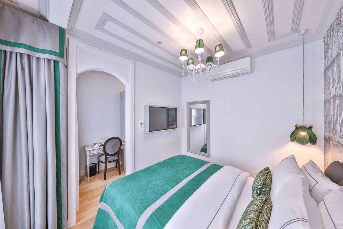 A bedroom with a green and white striped bedspread, a desk with a chair, a mirror, and a chandelier.