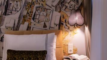 Une chambre à coucher avec un lit, des oreillers, une table de chevet sur laquelle est posé un livre ouvert, et un mur orné d’un motif décoratif.