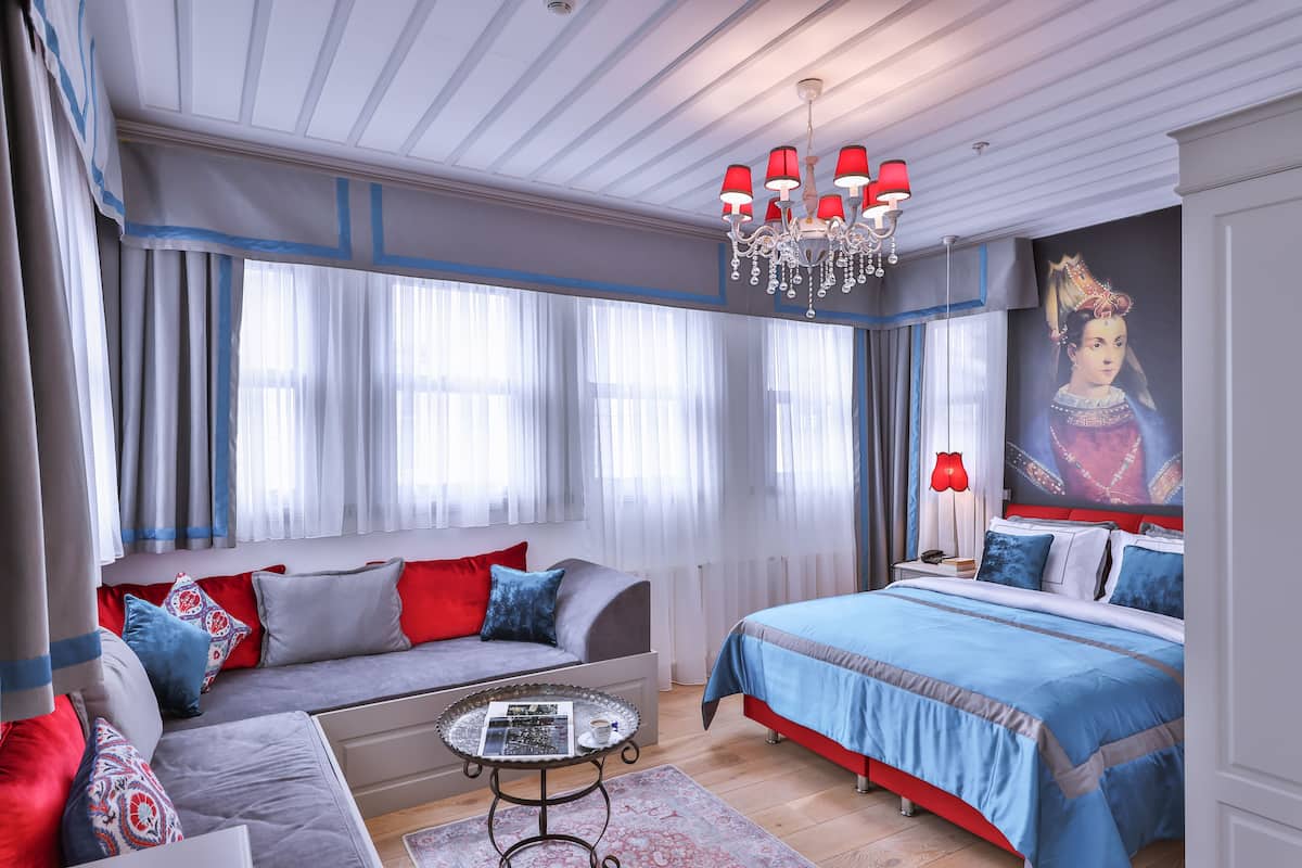 A modern bedroom with a large bed, a sofa, a small round table, and a chandelier.