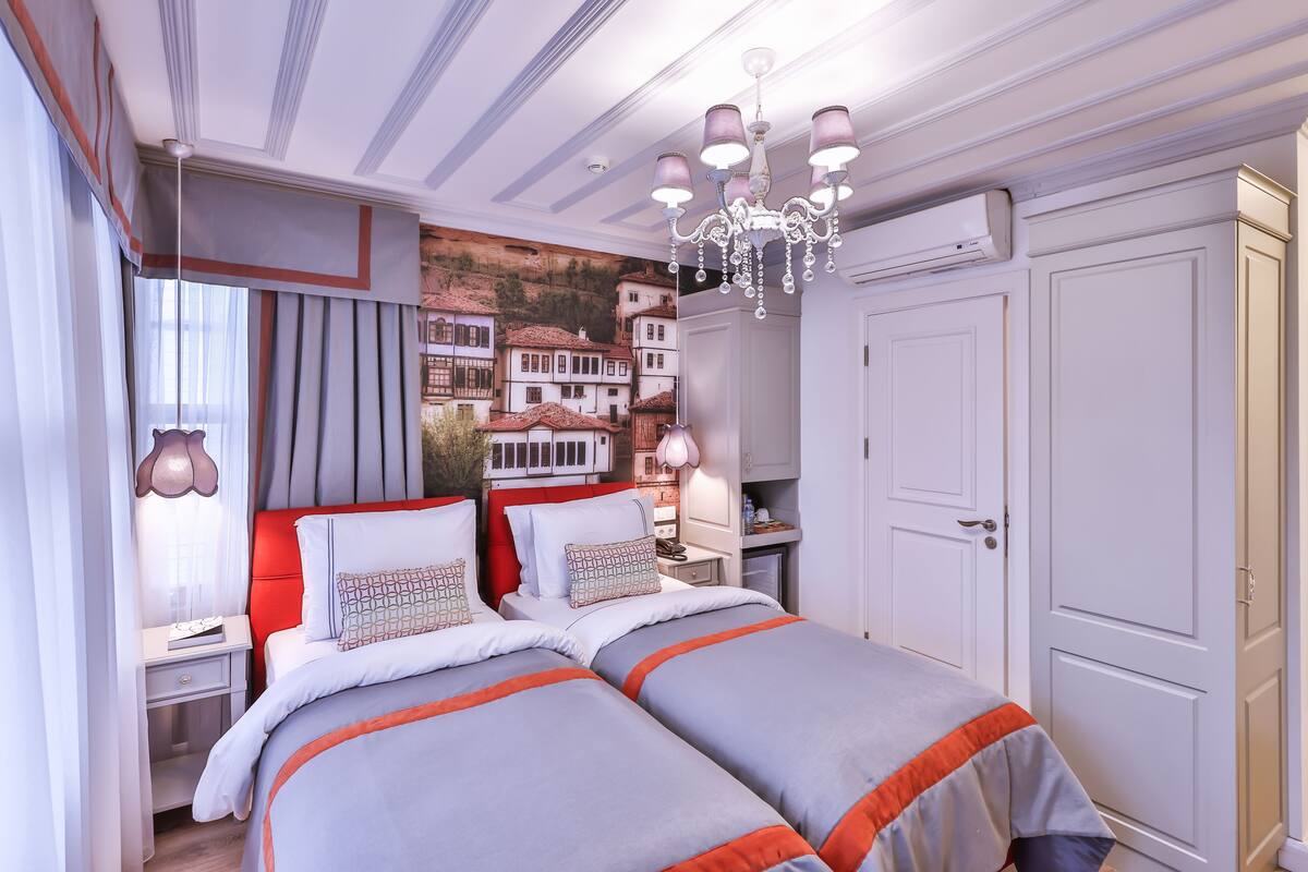 A double bed with two pillows, a nightstand, a lamp, and a wall mural of houses.