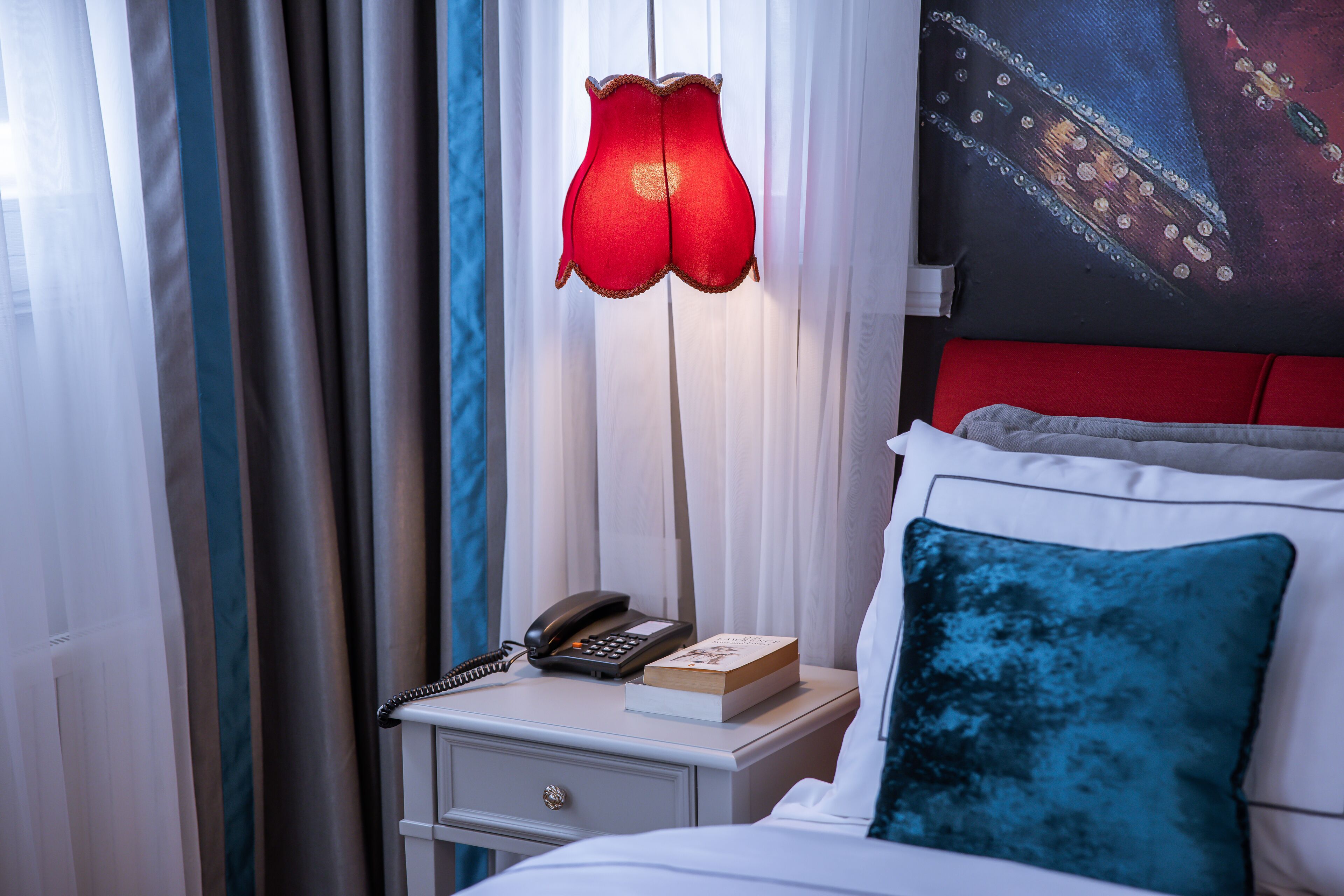 A neatly made bed with a blue pillow, a bedside lamp, a book, and a phone on a nightstand.