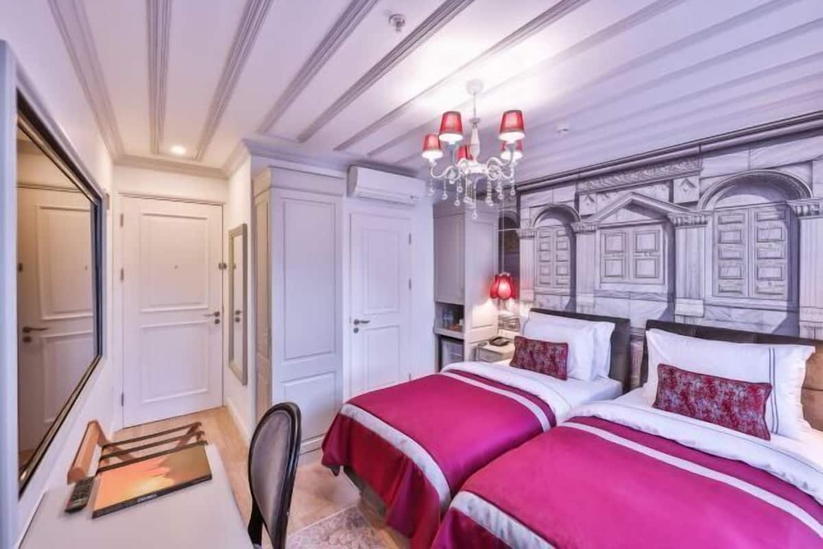 A hotel room with two beds, a chandelier, a mirror, and a door.