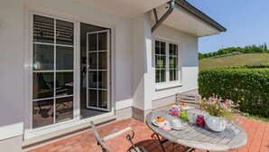 Eine Terrasse mit Esstisch, großen Fenstern und Blick auf eine grüne Landschaft.