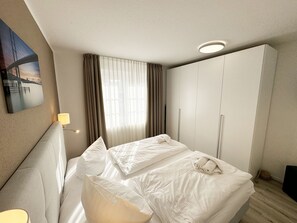 A hotel room with a bed, a wardrobe, a painting on the wall, and a window with curtains. - House A - Whg 01 with terrace - F: Lotsenberg Apartments with 8 apartments (Mönchgut)