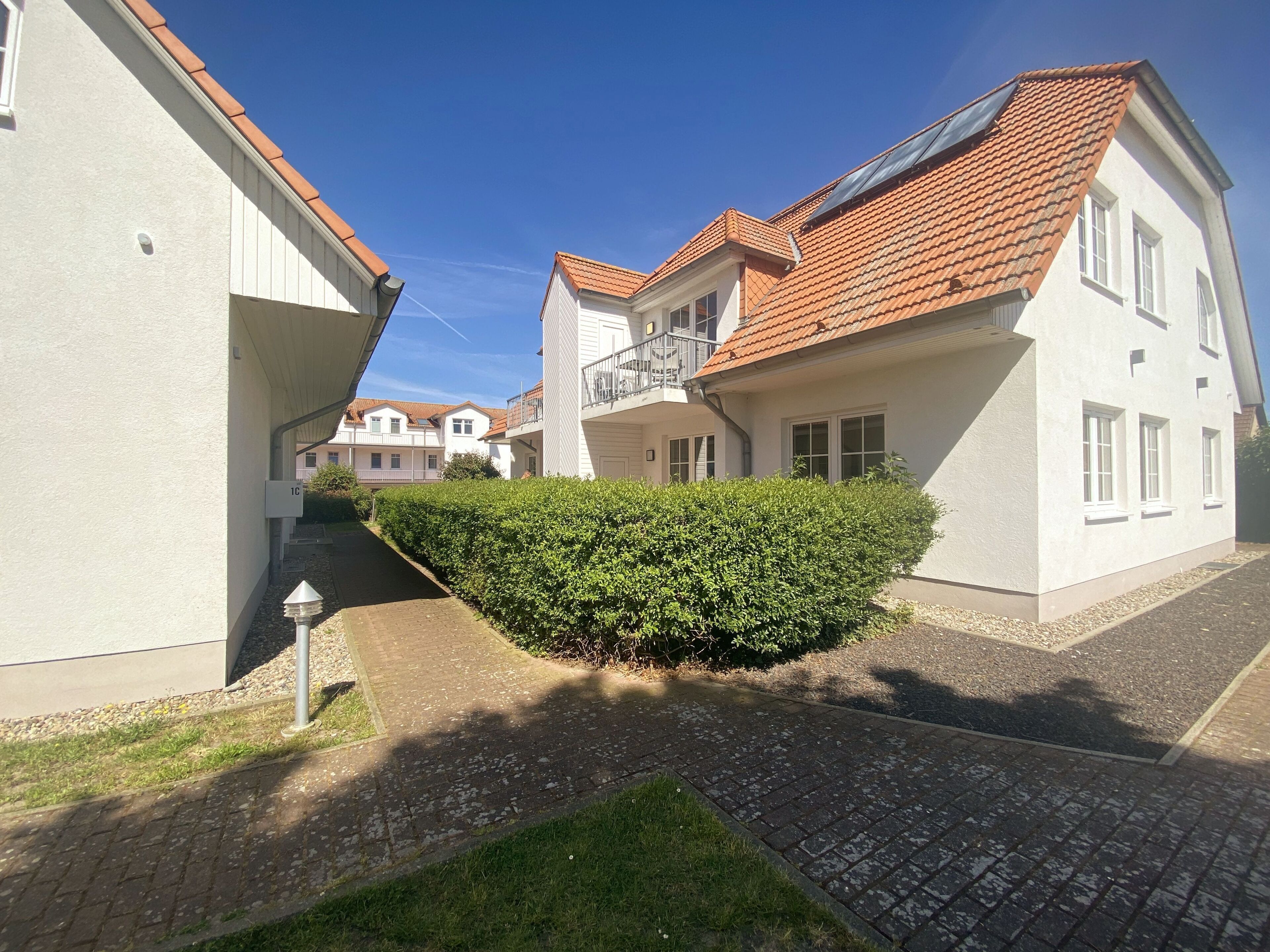 Un quartier résidentiel caractérisé par des bâtiments blancs, des toits recouverts de tuiles rouges et une haie bien entretenue.