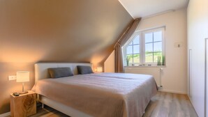 Ein Schlafzimmer mit einem großen Bett, einem Nachttisch, einem Fenster mit Vorhängen und einer Heizung.
