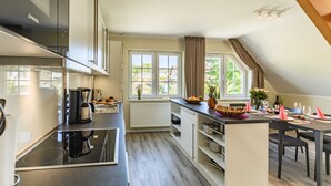 Eine moderne Küche mit einer zentralen Kochinsel, einem Essbereich mit Tisch und Stühlen sowie großen Fenstern mit Vorhängen.