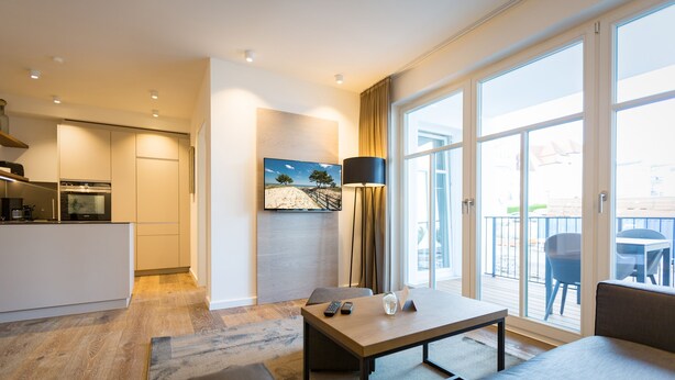 Ein modernes Hotelzimmer mit Küchenzeile, einem Essbereich mit Tisch und Stühlen sowie einer großen Glastür, die auf einen Außenbalkon führt.