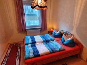 Une pièce avec un lit, une fenêtre avec des rideaux, un radiateur et une lampe.