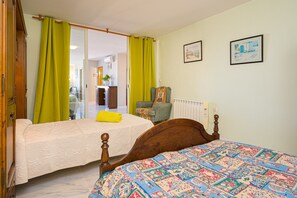 A bedroom with two beds, a chair, a radiator, and a door leading to another room. - Apartment 'Casa Meli' with Mountain View, Pool, Garden & Wi-Fi (Finestrat)