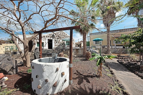 A traditional well, a tree, and a building with a balcony in a courtyard.