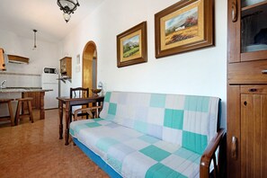 Un soggiorno con divano, arredi in legno, angolo cottura e due quadri appesi al muro.
