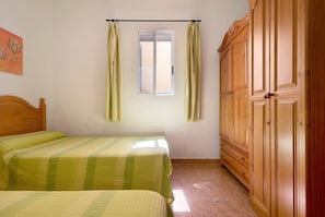 A bedroom with two beds, a window with curtains, and a wooden wardrobe.