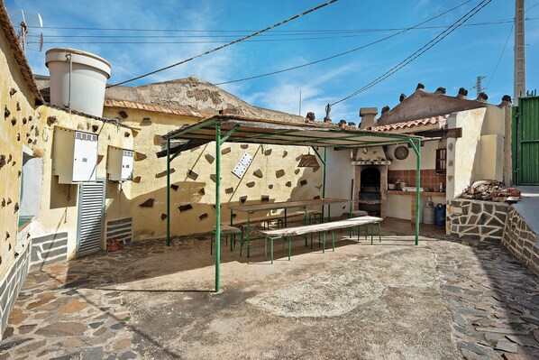 Ein Innenhof mit Steinboden, einer Bank, einem Tisch und einer grünen Pergola.
