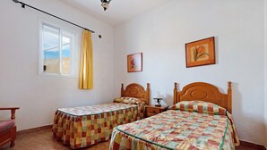 Un dormitorio con dos camas individuales, cabecero de madera, ventana con cortinas, mesita de noche y un cuadro colgado en la pared.