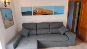 Ein graues Ecksofa in einem Raum mit Fliesenboden, einem Landschaftsbild an der Wand und einer Tür rechts.
